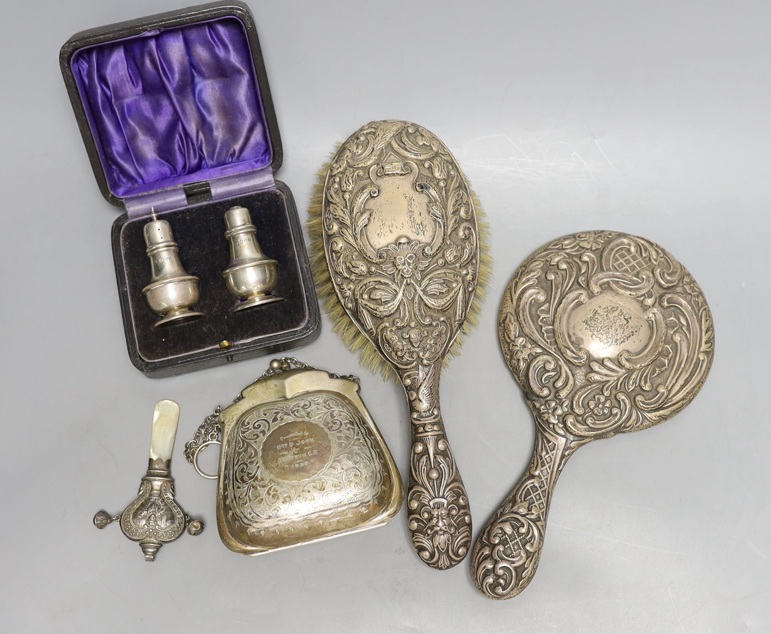 A cased pair of George V silver condiments, an engraved silver purse, silver mounted mirror and brush an a child's silver rattle.
